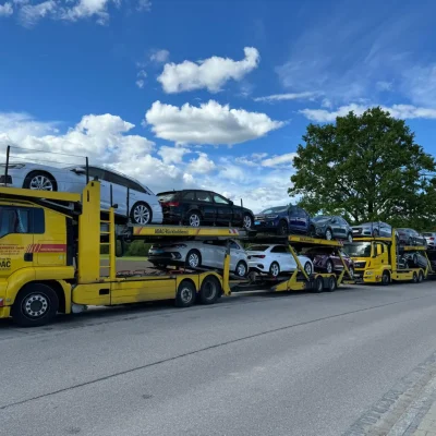 Mehrere gelbe ADAC-Autotransporter mit beladenen Neuwagen stehen aufgereiht am Straßenrand unter blauem Himmel mit Wolken. Die Szene zeigt einen typischen Fahrzeugkonvoi im Rahmen der professionellen Rückholdienste.